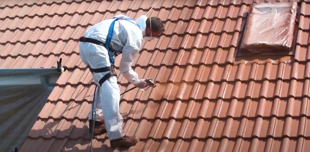 Technicien en harnais appliquant un traitement sur une toiture en tuiles