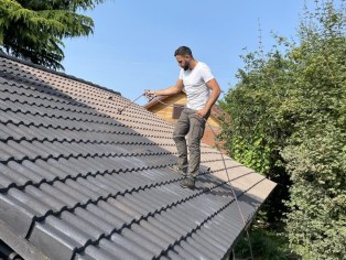 Couvreur appliquant un traitement sur une toiture en tuiles